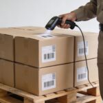 employe logistique scannant colis empiles sur palettes