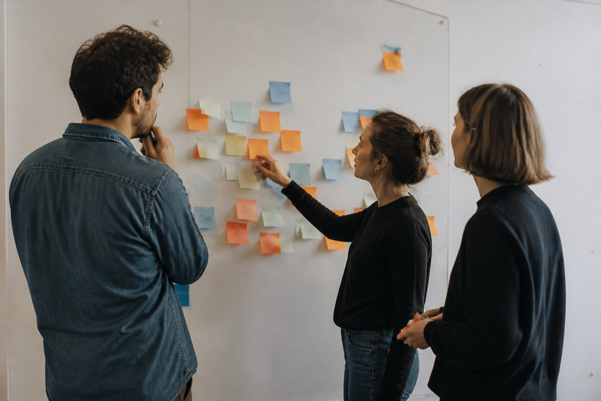 Trois collegues devant un tableau blanc couvert de notes